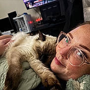 Yuki is registered to the contest to win money with this photo: cat, person, glasses, smile, face, freckles, nose_ring, hand, blanket, indoor, furniture, technology, computer, screen, cuddling, pet, resting, cozy, comfort, closeup