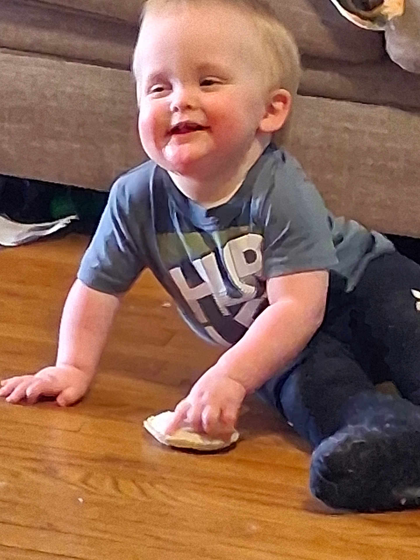 Brycen is registered to the contest to win money with this photo: toddler, child, smiling, sitting, floor, wooden_floor, indoor, casual_clothing, short_sleeves, snack, hand, face, happy, couch, home, person, young_child, cute, playful, light