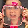 toddler, child, face, plastic_container, car_seat, red_shirt, hands, funny_expression, wide_eyes, tongue_out, hair_tie, pink, colorful, seatbelt, closeup, indoors, playful, cute, person, baby