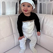 Khalis a rejoint le concours — aidez-le/la à gagner de superbes lots ! baby, child, smiling, sitting, indoors, clothing, hat, footed_pajamas, face, happy, cute, infant, person, furniture, cushion, white, black, portrait, headwear, cozy