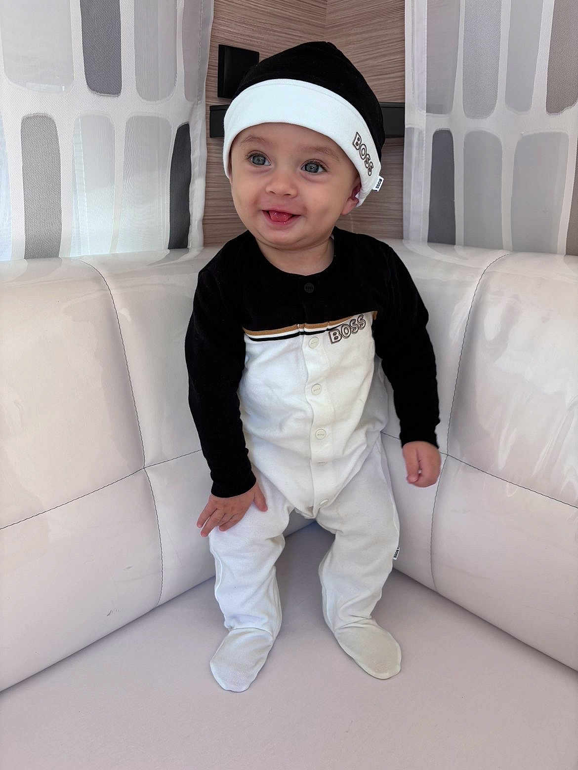 Khalis a rejoint le concours — aidez-le/la à gagner de superbes lots ! baby, child, smiling, sitting, indoors, clothing, hat, footed_pajamas, face, happy, cute, infant, person, furniture, cushion, white, black, portrait, headwear, cozy