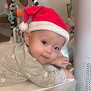 Alexander joined the competition — help win amazing prizes! baby, infant, santa_hat, gray_clothing, star_pattern, indoor, toy, air_purifier, curious_expression, face, child, cute, holiday, festive, soft_surface, hand, lying_down, headwear, smile, warm_lighting