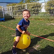 Yanis a rejoint le concours — aidez-le/la à gagner de superbes lots ! blue_sky, boy, child, fence, fun, grass, greenery, happy, hopper_ball, outdoor, play, recreation, shadow, shoes, shorts, smiling, sunlight, tree, tshirt, yellow_ball