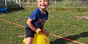 Yanis a rejoint le concours — aidez-le/la à gagner de superbes lots ! blue_sky, boy, child, fence, fun, grass, greenery, happy, hopper_ball, outdoor, play, recreation, shadow, shoes, shorts, smiling, sunlight, tree, tshirt, yellow_ball