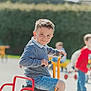 Yanis a rejoint le concours — aidez-le/la à gagner de superbes lots ! activity, background, blur, boy, casual_clothing, child, daylight, face, hair, handlebar, outdoor, person, playground, shorts, smile, sneakers, sunny, toy, tricycle, wheel