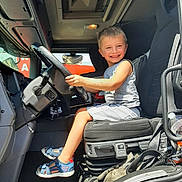 Yanis participe au concours pour gagner de l'argent avec cette photo : boy, casual, child, clothing, dashboard, driving, footwear, gloves, happy, interior, portrait, sandals, seat, small, smile, steering_wheel, sunlight, transport, truck, vehicle