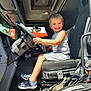 boy, casual, child, clothing, dashboard, driving, footwear, gloves, happy, interior, portrait, sandals, seat, small, smile, steering_wheel, sunlight, transport, truck, vehicle