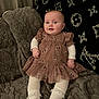 Rylie is registered to the contest to win money with this photo: baby, infant, child, dress, tights, blanket, plush, smile, face, cute, indoor, comfort, fabric, pattern, cozy, seated, person, young_child, clothing, soft