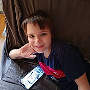 Cameronn a rejoint le concours — aidez-le/la à gagner de superbes lots ! boy, casual_clothing, child, couch, face, furniture, hair, hand, happy, home, indoor, person, portrait, relaxed, screen, sitting, smartphone, smiling, technology, young