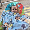 Ezeriel joined the competition — help win amazing prizes! baby, baby_seat, blanket, cartoon, child, clothing, colorful, concrete_floor, face, footwear, hand, happy, infant, outdoor, person, plush, porch, railing, smiling, sunlight