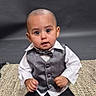 baby, black_pants, bow_tie, child, curious, cute, expression, floor, formal_wear, indoor, portrait, rug, sitting, small, studio, tuxedo, vest, white_shirt, white_shoes, young