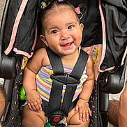 Lilah joined the competition — help win amazing prizes! baby, car_seat, smiling, child, safety_harness, hair_clips, colorful, striped_clothing, happy, cute, infant, indoors, seat, toy, person, portrait, childcare, secure, expression, closeup