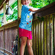 Grayleigh joined the competition — help win amazing prizes! child, girl, smiling, outdoor, porch, wooden_railing, greenery, summer_clothing, shorts, tshirt, happy, nature, daylight, sandals, balcony, playful, cute, sunlight, wooden_floor, casual