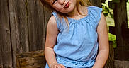 Grayleigh is registered to the contest to win money with this photo: bench, blue_dress, casual, child, crossed_legs, cute, daylight, girl, greenery, happy, nature, outdoor, playful, portrait, red_bench, sitting, smiling, summer, wood, wooden_fence