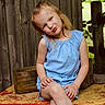Grayleigh is registered to the contest to win money with this photo: child, girl, blue_dress, crossed_legs, wooden_fence, bench, outdoor, playful, smiling, nature, greenery, summer, portrait, casual, cute, sitting, daylight, wood, red_bench, happy