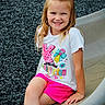 child, girl, smile, playground, slide, hair_bow, white_shirt, pink_shorts, outdoor, happy, sitting, kindergarten, casual_clothing, young, person, daylight, cute, play, fun, park