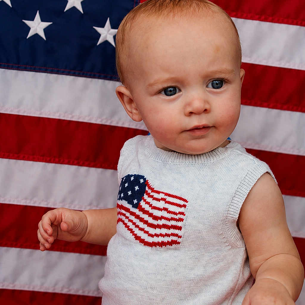 James is registered to the contest to win money with this photo: toddler, child, american_flag, patriotic, blue_eyes, sleeveless_outfit, knitted_clothing, red_white_blue, flag_background, cute, portrait, young_child, baby, indoor, expression, skin, hand, head, person, photography