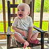 baby, child, rocking_chair, wood, porch, smiling, happy, outdoor, sunlight, greenery, summer, infant, clothing, barefoot, sitting, person, nature, daylight, wooden_furniture, cute