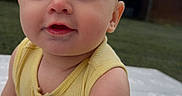 James is registered to the contest to win money with this photo: arm, baby, building, child, close_up, curious, cute, daylight, face, grass, happy, infant, outdoor, patterned_pants, person, portrait, skin, smiling, yellow_top, young_child
