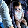 baby, car_seat, sunglasses, white_clothing, infant, child, seatbelt, person, legs, arm, casual, footwear, indoor, cute, young, relaxed, fashion, accessory, portrait, toddler