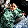 baby, child, car_seat, green_clothing, dinosaur_print, blanket, blue_blanket, floral_pattern, car_interior, seat, person, infant, cute, lying_down, portrait, young_child, smiling, comfortable, casual, indoors