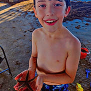 Marcus is registered to the contest to win money with this photo: child, boy, smiling, portrait, beach, seaside, sand, ocean, starfish, marine_life, swimwear, wet_hair, outdoor, summer, sunlight, blue_shorts, red_bucket, beach_toys, playful, nature