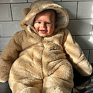 Thiago joined the competition — help win amazing prizes! baby, child, smile, face, fur_clothing, hood, teddy_bear_costume, cute, indoors, tile_wall, sunlight, shadow, portrait, warm, soft_texture, person, infant, seated, happy, cozy