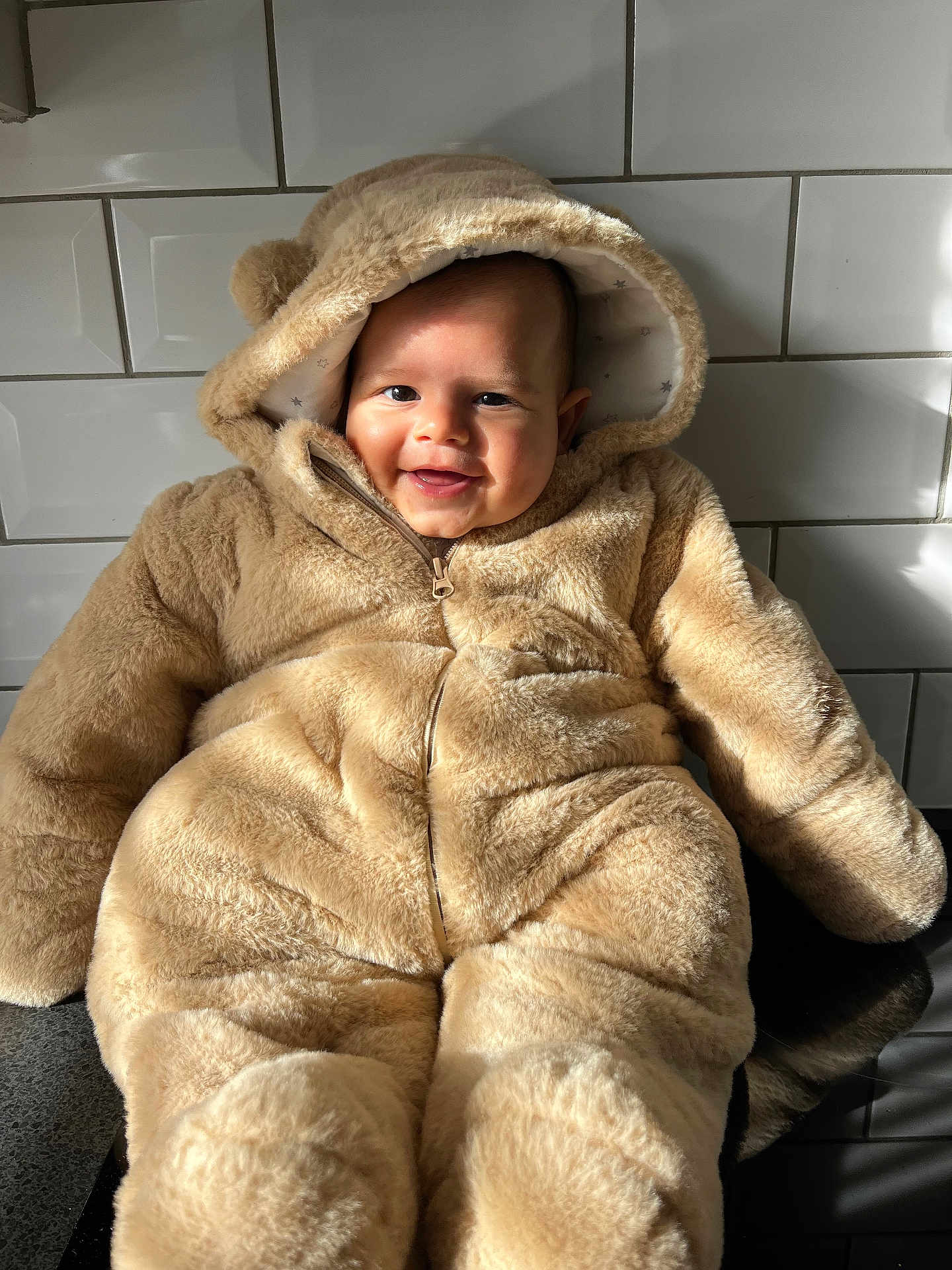 Thiago joined the competition — help win amazing prizes! baby, child, smile, face, fur_clothing, hood, teddy_bear_costume, cute, indoors, tile_wall, sunlight, shadow, portrait, warm, soft_texture, person, infant, seated, happy, cozy