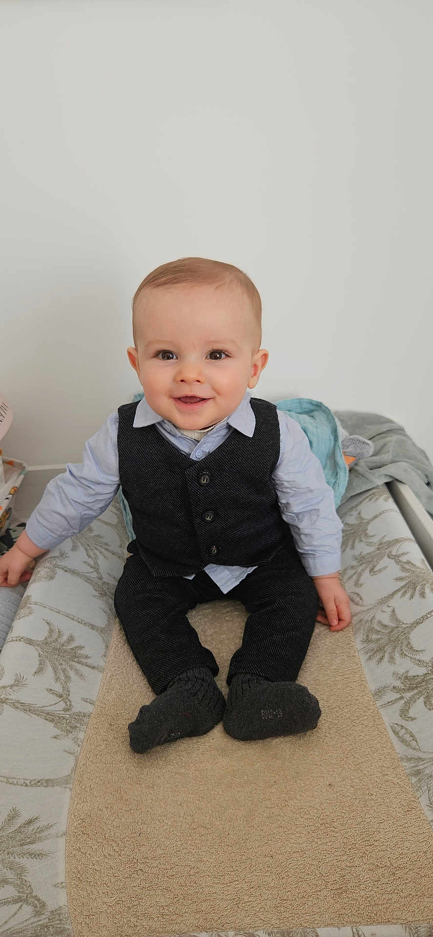 Jules participe au concours pour gagner de l'argent avec cette photo : baby, child, smiling, sitting, indoor, vest, shirt, sock, changing_table, blanket, happy, portrait, cute, infant, clothing, face, person, furniture, home, young