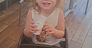 Echo is registered to the contest to win money with this photo: barefoot, blonde_hair, blue_eyes, casual_clothing, chairs, child, cup, dining_area, drink, happy, high_chair, indoor, portrait, restaurant, seated, smiling, sunlight, table, toddler, wooden_floor
