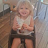 child, toddler, smiling, blonde_hair, blue_eyes, high_chair, cup, drink, restaurant, dining_area, table, chairs, wooden_floor, indoor, sunlight, portrait, seated, happy, casual_clothing, barefoot