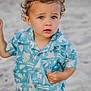 toddler, child, beach, sand, blue_shirt, curly_hair, outdoor, summer, portrait, casual_clothing, cute, young_child, expression, person, sunlight, vacation, nature, standing, fashion, small_person