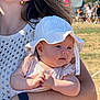 baby, child, hat, white_hat, adult, arm, watch, earring, outdoor, sunlight, grass, people, crowd, summer, portrait, closeup, holding, clothing, person, daytime
