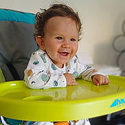 Ayden a rejoint le concours — aidez-le/la à gagner de superbes lots ! baby, child, smile, high_chair, curly_hair, pajamas, indoor, happy, face, infant, yellow, playful, young_child, furniture, seat, person, cute, expression, closeup, portrait