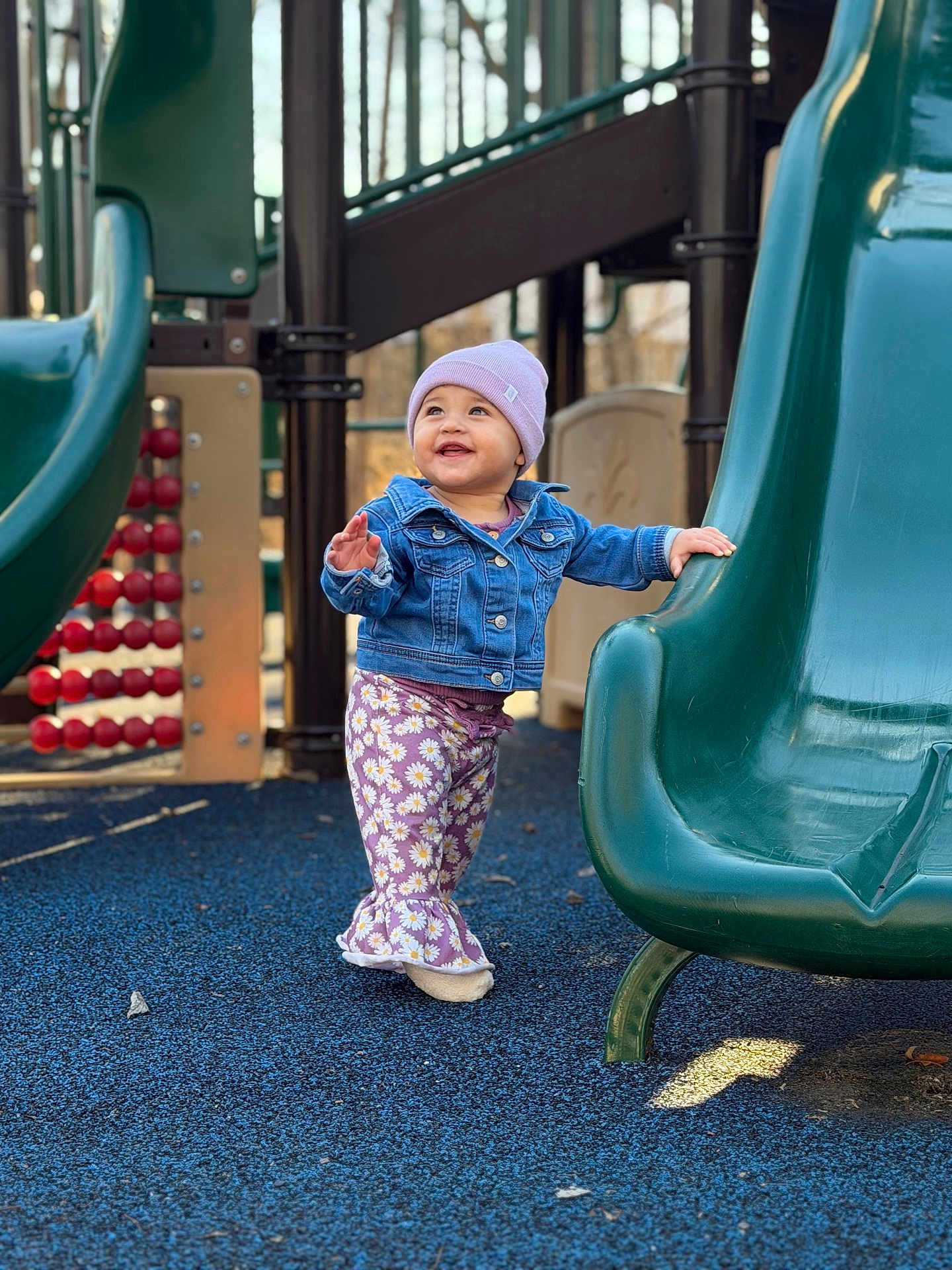 Ivanna is registered to the contest to win money with this photo: toddler, child, playground, slide, denim_jacket, beanie, purple_pants, smiling, outdoor, play, happy, clothing, person, daylight, plastic_slide, blue_floor, walking, cute, young_child, fun