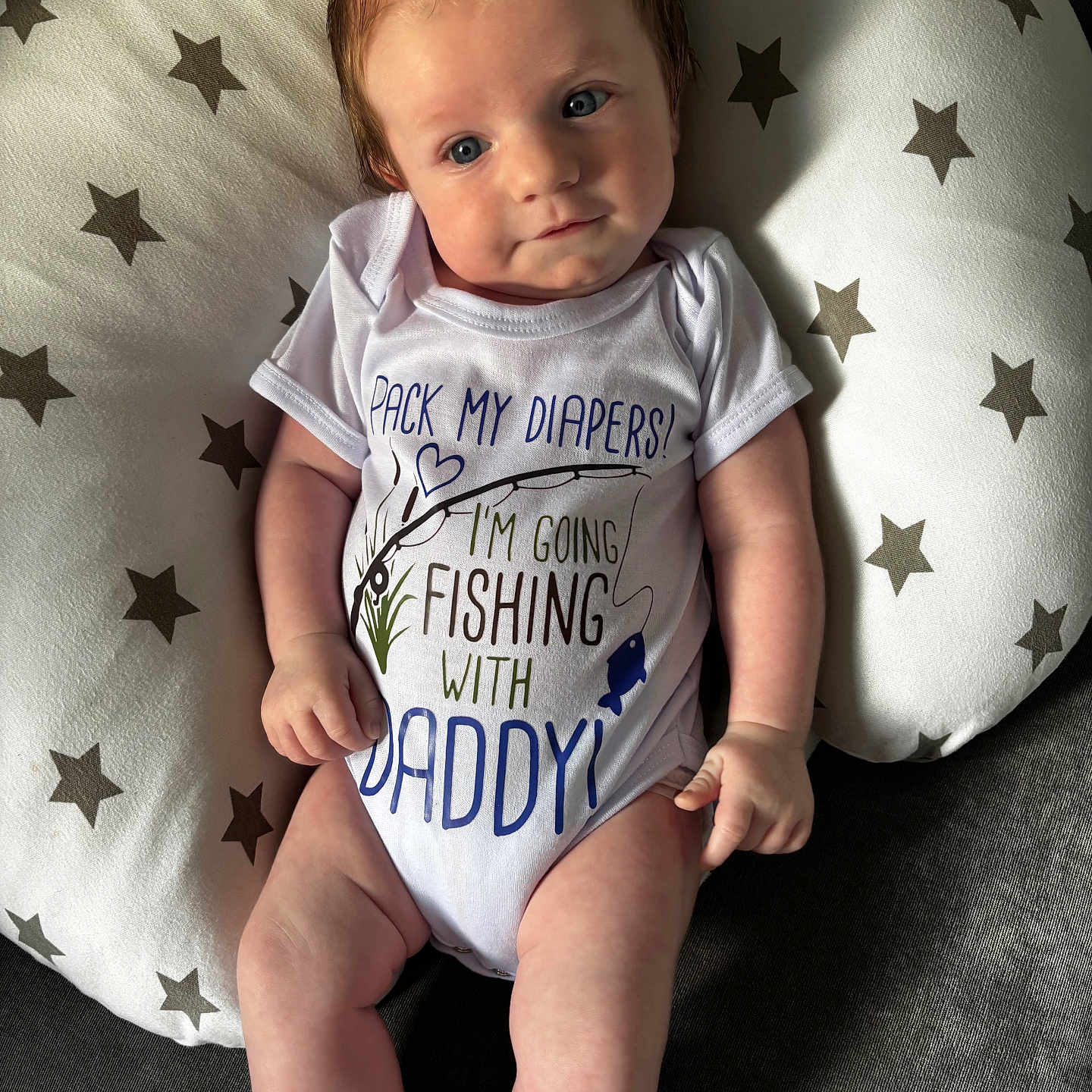 Max is registered to the contest to win money with this photo: baby, blue_eyes, child, clothing, cute, expression, face, hair, humor, indoor, infant, lying_down, onesie, person, pillow, skin, socks, soft_lighting, stars, text_on_clothing