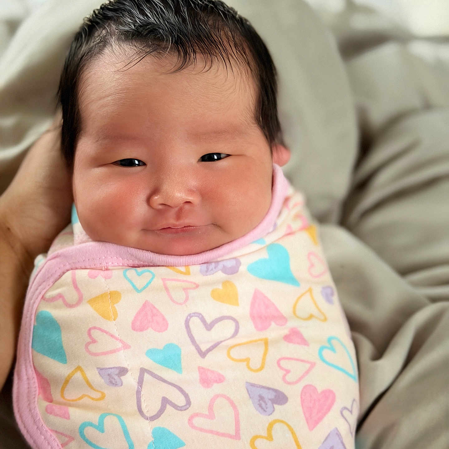 Juni Kim joined the competition — help win amazing prizes! baby, infant, swaddle, heart_pattern, smile, face, cute, newborn, wrapped, soft, cozy, person, child, indoors, closeup, skin, hair, pink, pastel_colors, comfortable