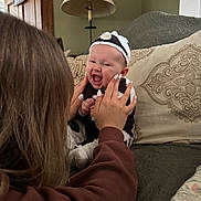 Beverly joined the competition — help win amazing prizes! baby, blanket, brown_hair, child, clothing, couch, face, hands, happy, headwear, home, indoor, lamp, nails, pattern, person, pillow, sitting, smile, woman