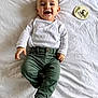baby, infant, smiling, white_clothing, green_pants, lying_down, milestone_sign, 5_months, happy, cute, child, person, white_sheet, sock, casual_wear, portrait, indoor, young_child, baby_boy, cheerful