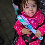 toddler, child, stroller, pink_raincoat, polka_dots, toy, glowing_toy, curly_hair, blue_eyes, outdoor, seatbelt, happy, cute, portrait, hands, face, smile, baby, clothing, playful