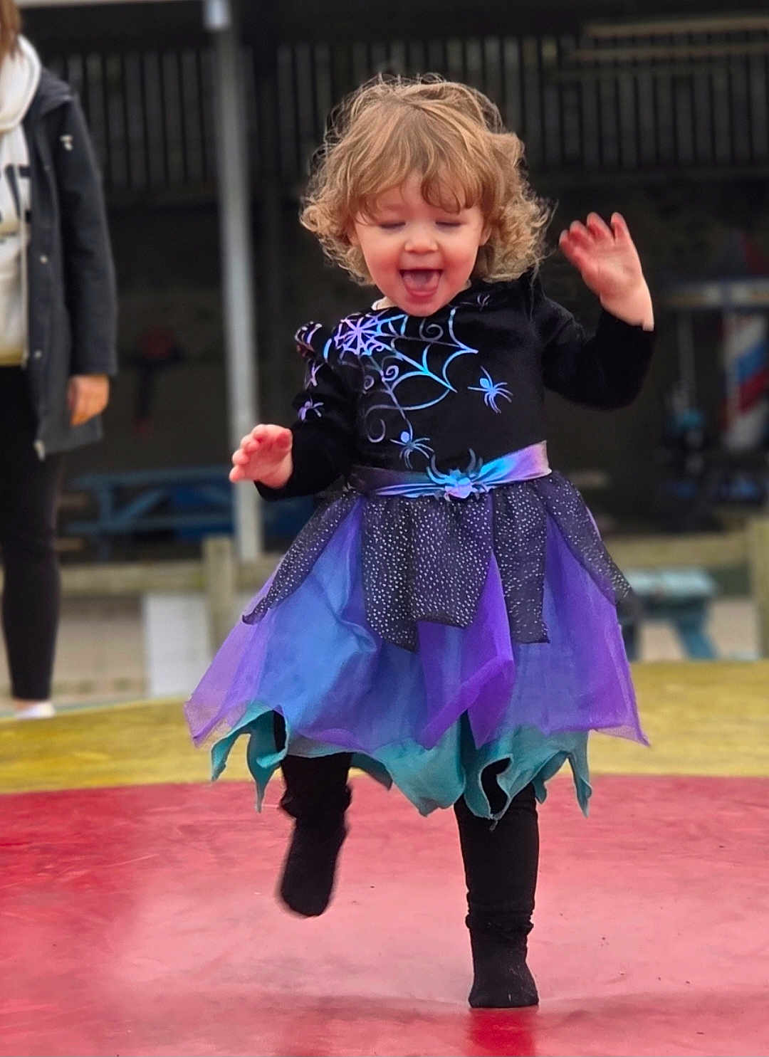 Stella is registered to the contest to win money with this photo: toddler, child, girl, curly_hair, purple_dress, blue_dress, spider_web, outdoor, playful, jumping, smiling, happy, person, fashion, costume, leggings, fun, movement, joy, blurred_background