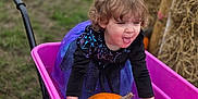 Stella joined the competition — help win amazing prizes! child, pumpkin, wheelbarrow, purple_dress, outdoor, grass, hay_bales, tongue_out, playful, curly_hair, autumn, dirt, muddy_hands, fall, toy, fun, person, smiling, nature, seasonal