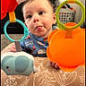 Bryson is registered to the contest to win money with this photo: baby, infant, child, tongue_out, playful, toy, elephant_toy, orange_toy, hanging_toy, patterned_cushion, indoor, laundry_basket, curtains, carpet, blue_clothing, rescue_squad_print, closeup, face, expression, cute