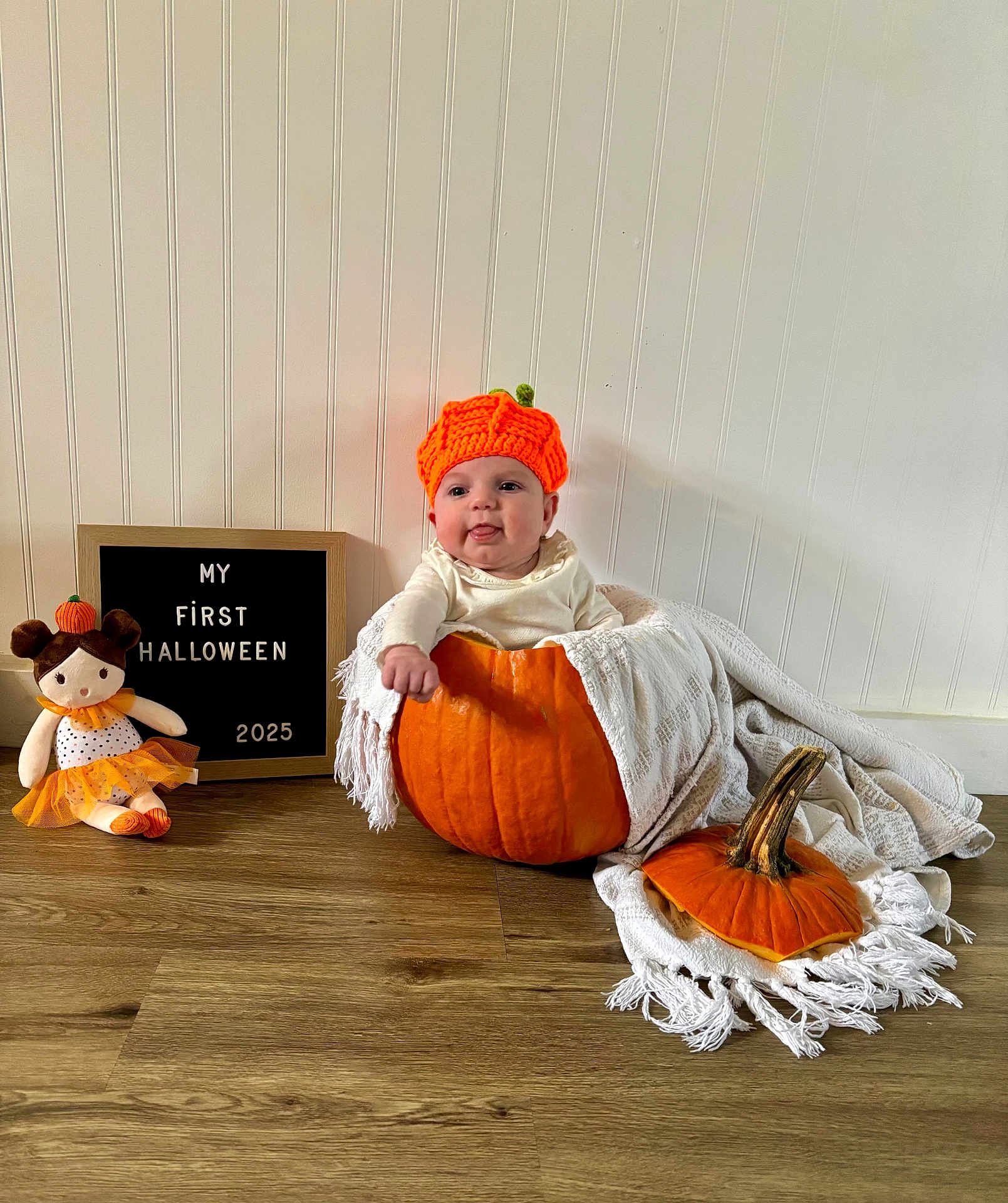 Kinsley joined the competition — help win amazing prizes! baby, pumpkin, orange_hat, blanket, doll, sign, wooden_floor, white_wall, halloween, cute, infant, costume, holiday, indoors, child, smiling, decor, festive, portrait, seasonal