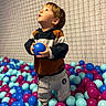 Naël participe au concours pour gagner de l'argent avec cette photo : toddler, child, ball_pit, blue_ball, colorful_balls, net, indoor, play, curious, clothing, hoodie, pants, portrait, smiling, young_child, toy, recreation, activity, fun, kid