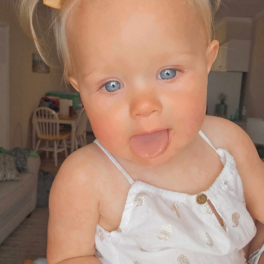 Maggie joined the competition — help win amazing prizes! baby, blue_eyes, bows, cartoon_stickers, child, cute, dining_chair, face, floor, hand, indoor, living_room, patterned_clothing, person, pigtails, shell, starfish, table, tongue_out, white_clothing