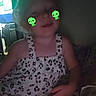 child, indoor, leopard_print, dress, sitting, face_stickers, green_text, dim_light, window, curtain, patterned_fabric, young_child, cute, playful, dinosaur_sticker, smiling, casual, portrait, colorful, fun