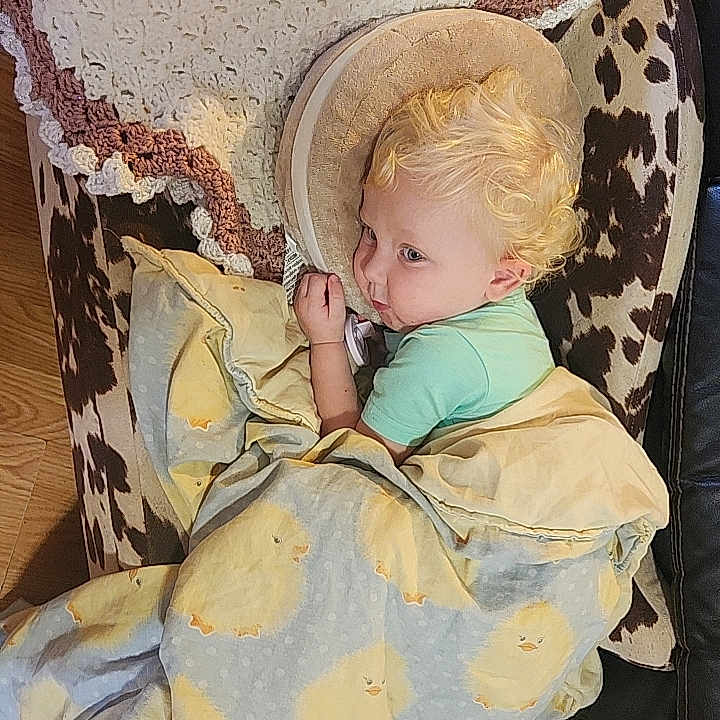 Madilyn is registered to the contest to win money with this photo: toddler, child, blanket, curly_hair, chair, cow_print, crocheted_throw, indoor, wooden_floor, cozy, cute, portrait, resting, yellow_chicks, clothing, face, person, furniture, soft_lighting, home