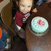 Rosalyn is registered to the contest to win money with this photo: toddler, child, birthday_cake, cake, high_chair, smile, happy, indoor, table, celebration, candle, sprinkles, maroon_shirt, person, wooden_table, floor, feet, family, party, food