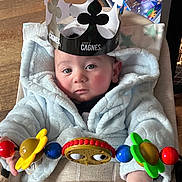 Harper a rejoint le concours — aidez-le/la à gagner de superbes lots ! baby, child, hoodie, crown, toy, flower, stroller, hand, face, blue, red, yellow, green, indoor, wood_floor, blanket, person, portrait, cute, expression
